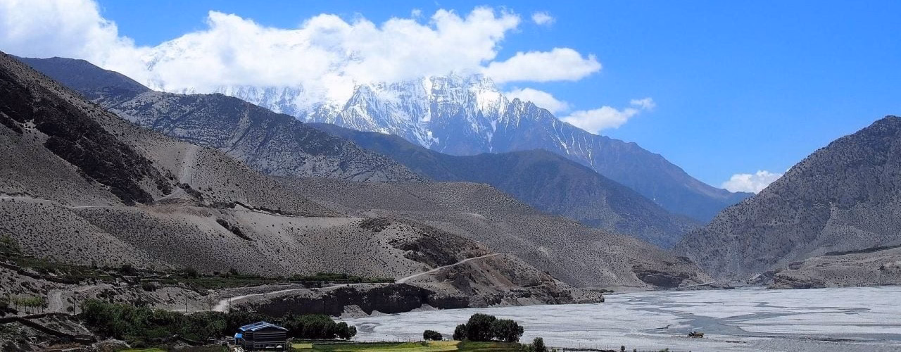A sweeping view of the snow-capped Himalayan peaks rising above the wide, arid valley of Upper Mustang